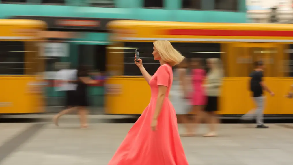 Žena s mobilem jde kolem tramvaje